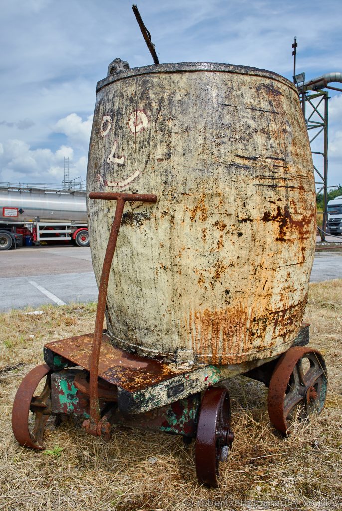 An old barrel sits on an old vintage barrow with steel wheels.